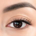 Close-up of a human eye with long, dark, curled eyelashes and a neatly shaped dark eyebrow on light skin.